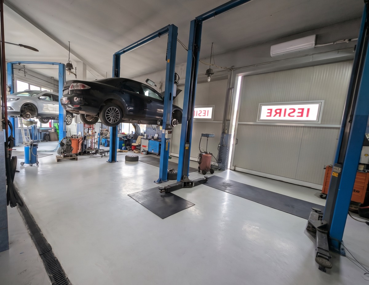 Interiorul atelierului autoFYG: două mașini ridicate pe elevatoare, podea gri curată și porțile de ieșire