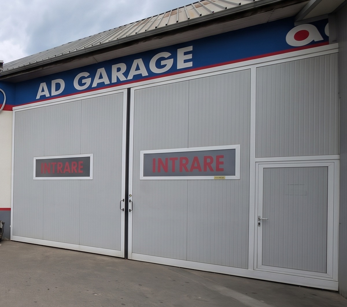 Fațada atelierului: porți gri cu inscripția INTRARE, sub o bandă albastră pe care scrie AD GARAGE